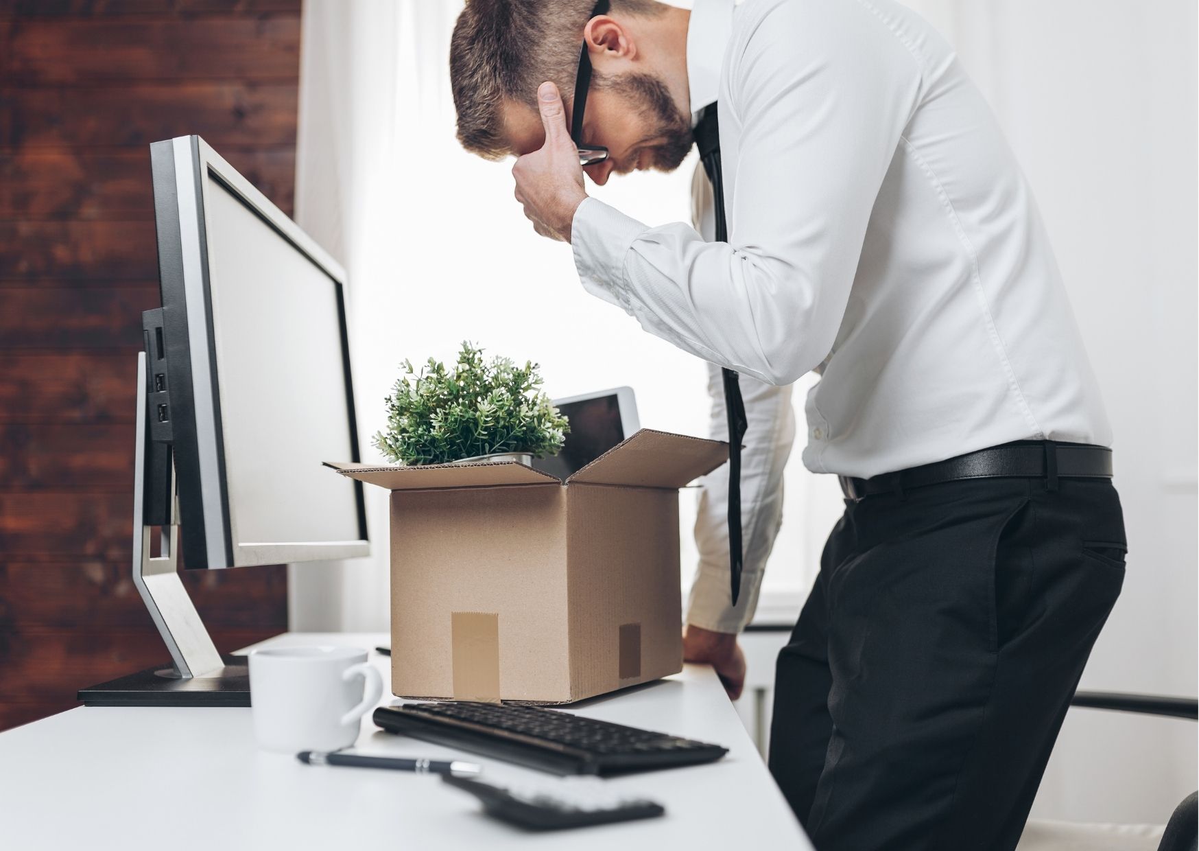 Man moedeloos voorovergebogen over zijn bureau. Spullen in doos. Net ontslagen.